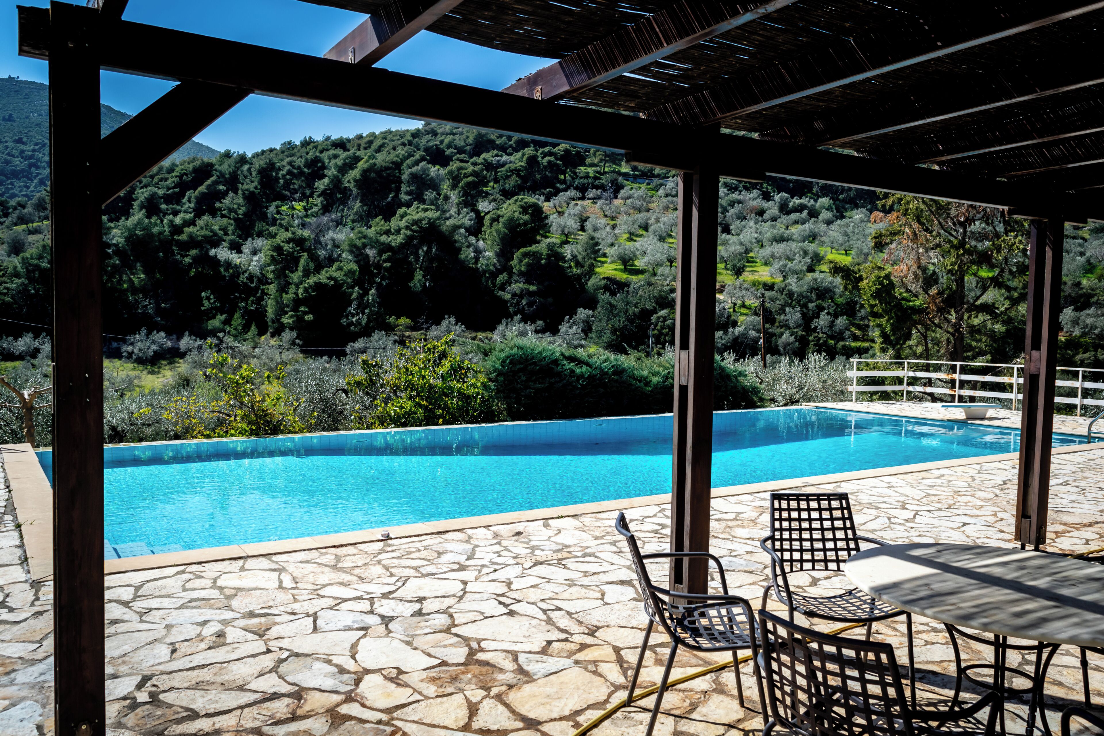 Una piscina con suelo de piedra, rodeada por una pérgola y una mesa con sillas.