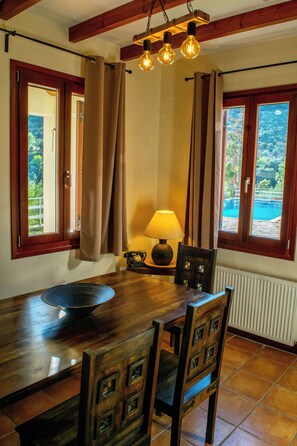 Ein Essbereich mit einem Holztisch, Stühlen, einer Lampe und Blick auf einen Swimmingpool durch die Fenster.
