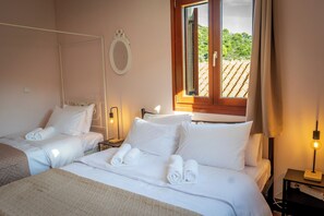 Ein Hotelzimmer mit zwei Betten, einem Nachttisch mit Lampe, einem Fenster mit Blick auf das Dach und einem an der Wand befestigten Spiegel.