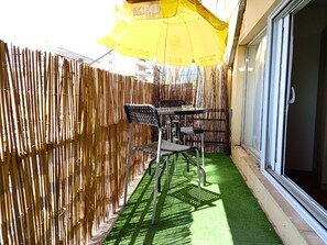 Eine Terrassenfläche mit Bambusumzäunung, einem Tisch mit Stühlen und einem gelben Sonnenschirm.