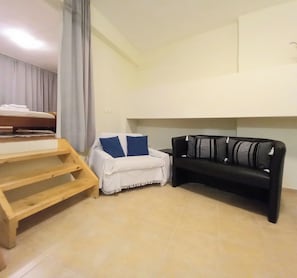 Ein Zimmer mit einem Bett, einem kleinen weißen Sofa mit blauen Kissen und einem schwarzen Sofa mit gestreiften Kissen.