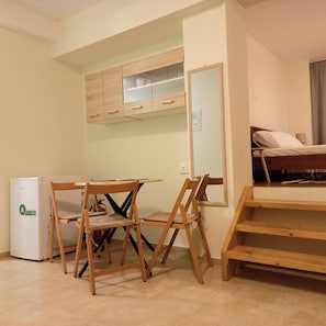 Ein kleines Zimmer mit einer Küchenzeile, einem Klapptisch, zwei Stühlen, einem Bett und einem Spiegel.