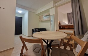 Een kamer met een ronde tafel en vier stoelen, een bed met hoofdeinde, een kledingkast en een deur naar een andere kamer.