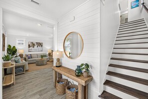 A modern living room with a staircase, wooden flooring, and a console table with decorative items. - New! 5BR Beach Family Retreat, Pool, Water Views, Pickleball, Dog-Friendly (Port St. Joe)
