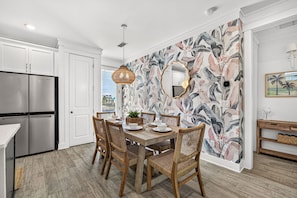 A dining area with a wooden table, wicker chairs, and a wall with a tropical leaf pattern. - New! 5BR Beach Family Retreat, Pool, Water Views, Pickleball, Dog-Friendly (Port St. Joe)