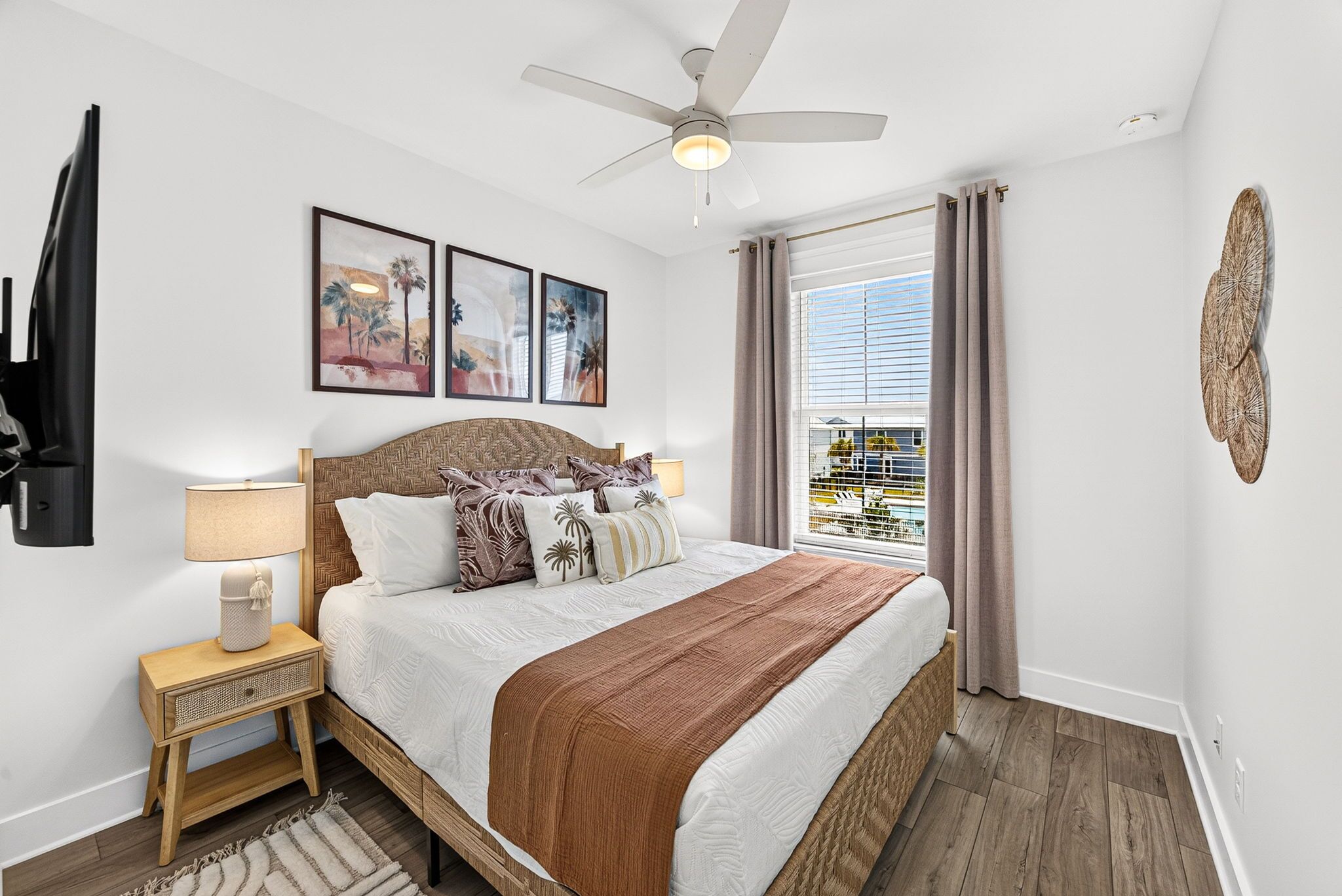 A bedroom with a bed, a nightstand, a lamp, a ceiling fan, and a window with curtains.
