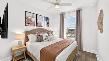 A bedroom with a bed, a nightstand, a lamp, a ceiling fan, and a window with curtains.