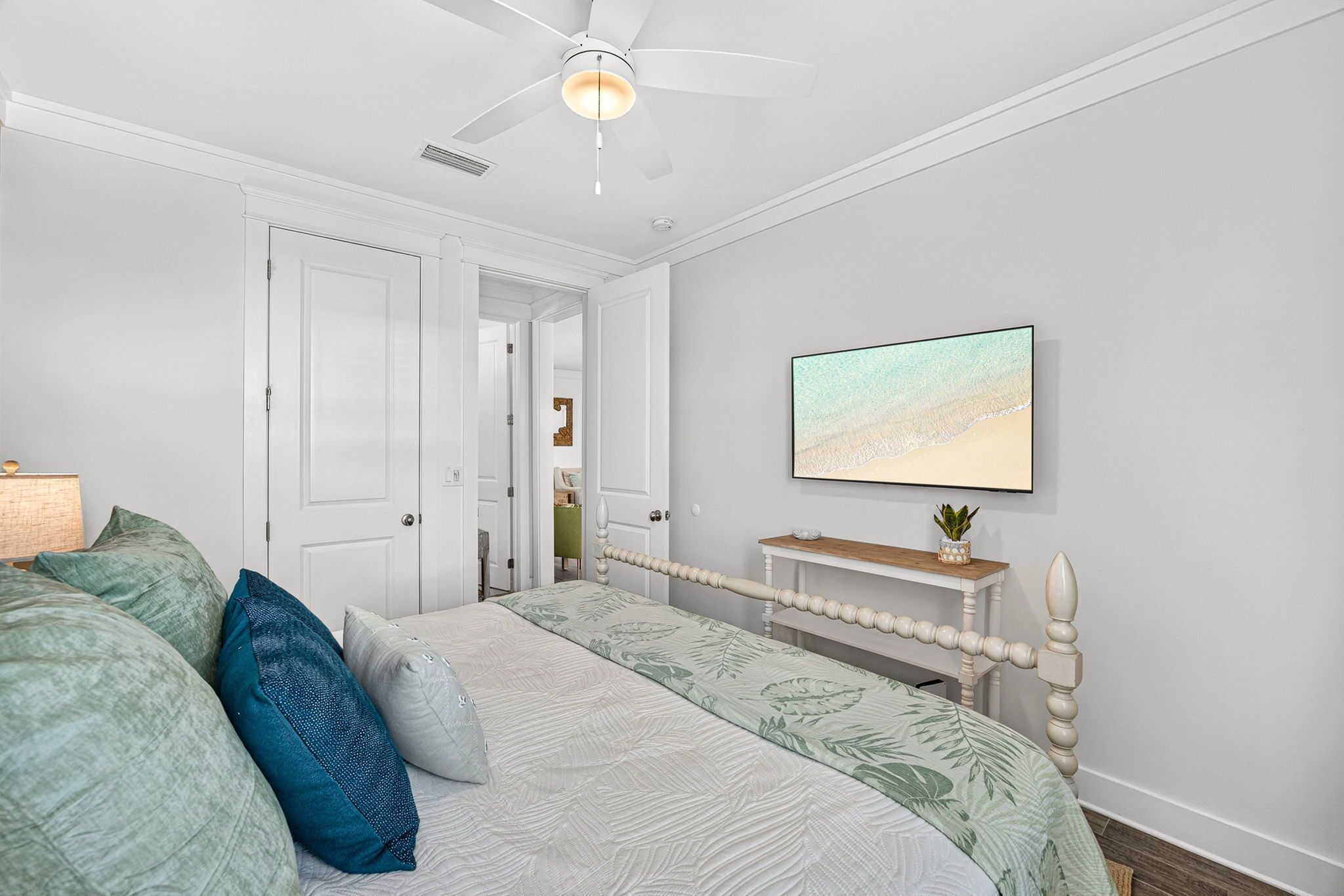 A bedroom with a bed, a ceiling fan, a bedside table, and a wall-mounted TV.