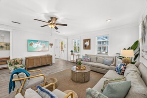Un salon spacieux doté d’un ventilateur de plafond, d’un grand téléviseur à écran plat, d’une table basse en bois et d’un coin salon confortable avec un canapé et des fauteuils.