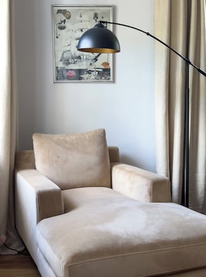A beige sofa in a room with a black floor lamp, a framed picture on the wall, and beige curtains. - Welcome to Golden Hour Bungalow — a cozy, mid-century surf retreat. (Carolina Beach)