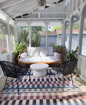 A covered outdoor seating area with a sofa and two chairs, a checkered rug, and potted plants. - Welcome to Golden Hour Bungalow — a cozy, mid-century surf retreat. (Carolina Beach)
