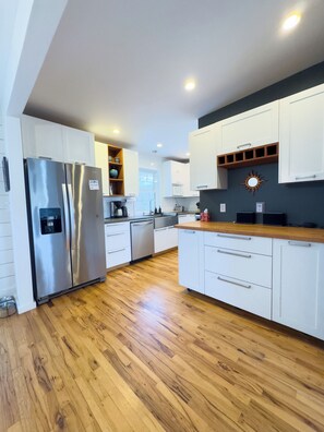 A modern kitchen with white cabinets, stainless steel appliances, and a wooden countertop. - Welcome to Golden Hour Bungalow — a cozy, mid-century surf retreat. (Carolina Beach)