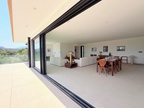 A modern interior with a dining area, sofa set, and a view through a glass door. - New contemporary villa with pool—5 bedrooms with en suite bathrooms—Ste Lucie de PV (Sainte Lucie de Porto Vecchio)