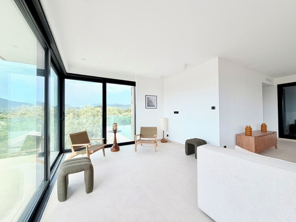 A modern living room with large windows, a sofa, two chairs, and a small table.