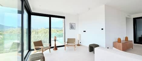 A modern living room with large windows, a sofa, two chairs, and a small table.