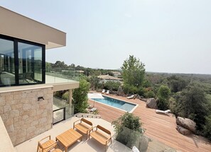 A modern outdoor deck with a pool, stone walls, and wooden furniture. - New contemporary villa with pool—5 bedrooms with en suite bathrooms—Ste Lucie de PV (Sainte Lucie de Porto Vecchio)