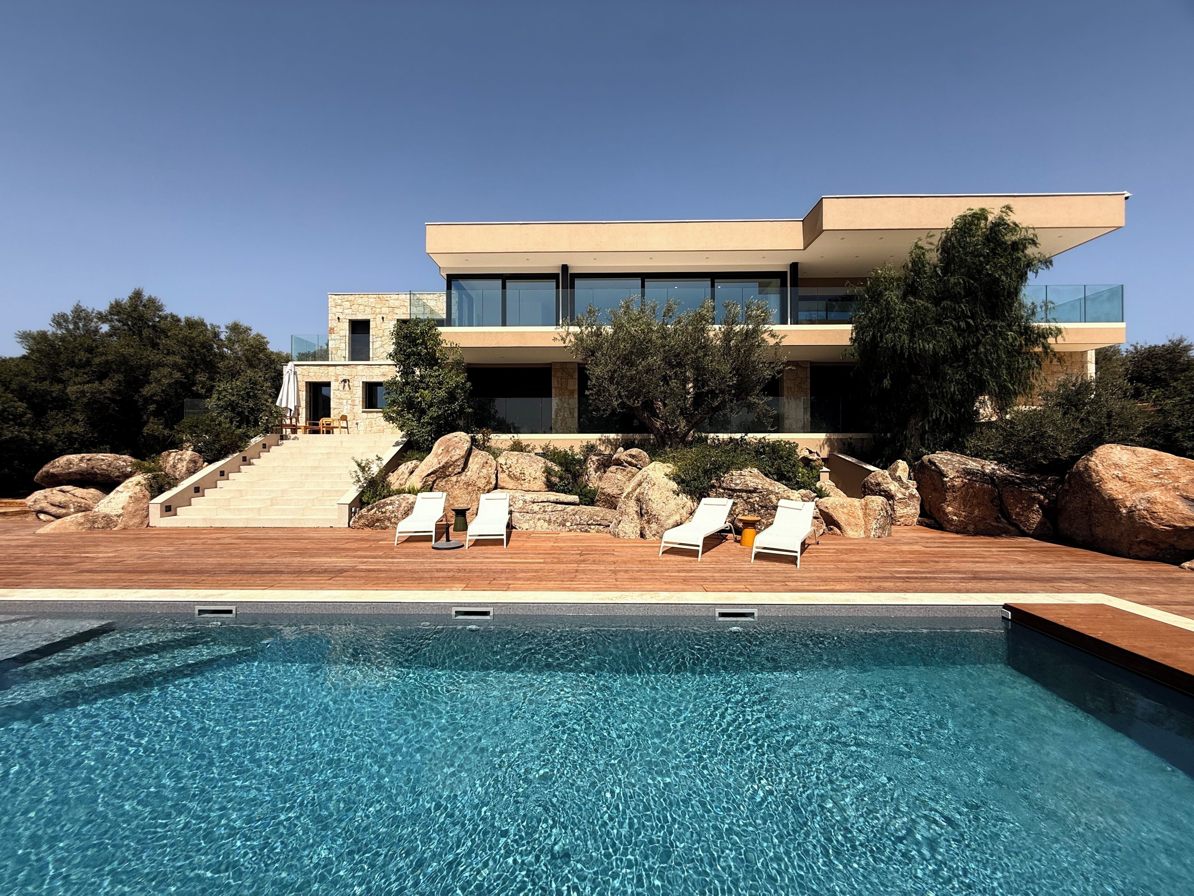 Ein modernes Haus mit Schwimmbad, Gartenmöbeln und großen Felsen.