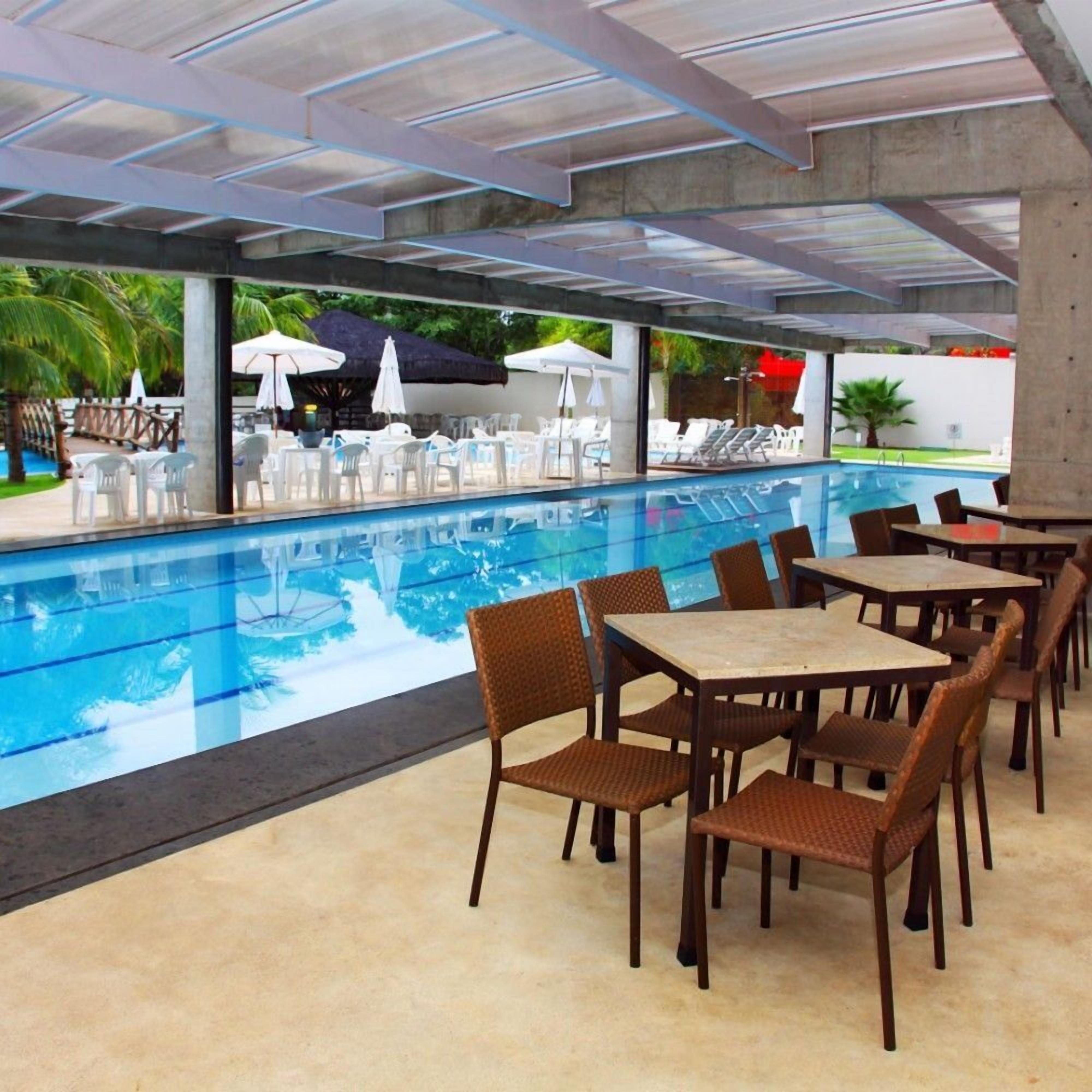 Uma área de piscina com espreguiçadeiras, mesas e guarda-sóis.