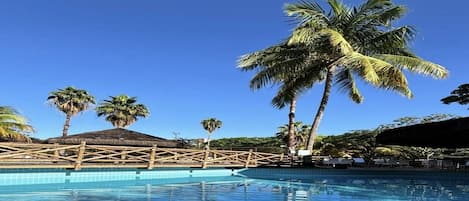 Une piscine avec une terrasse en bois et des palmiers en arrière-plan.