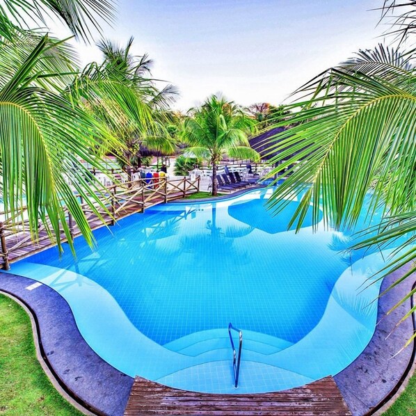 A swimming pool with a wooden deck and palm trees. - Hotel Le Jardin Best Western (Caldas Novas)