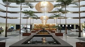 A spacious lobby with a central water feature, multiple palm trees, and a modern reception desk. - Hotel Le Jardin Best Western (Caldas Novas)