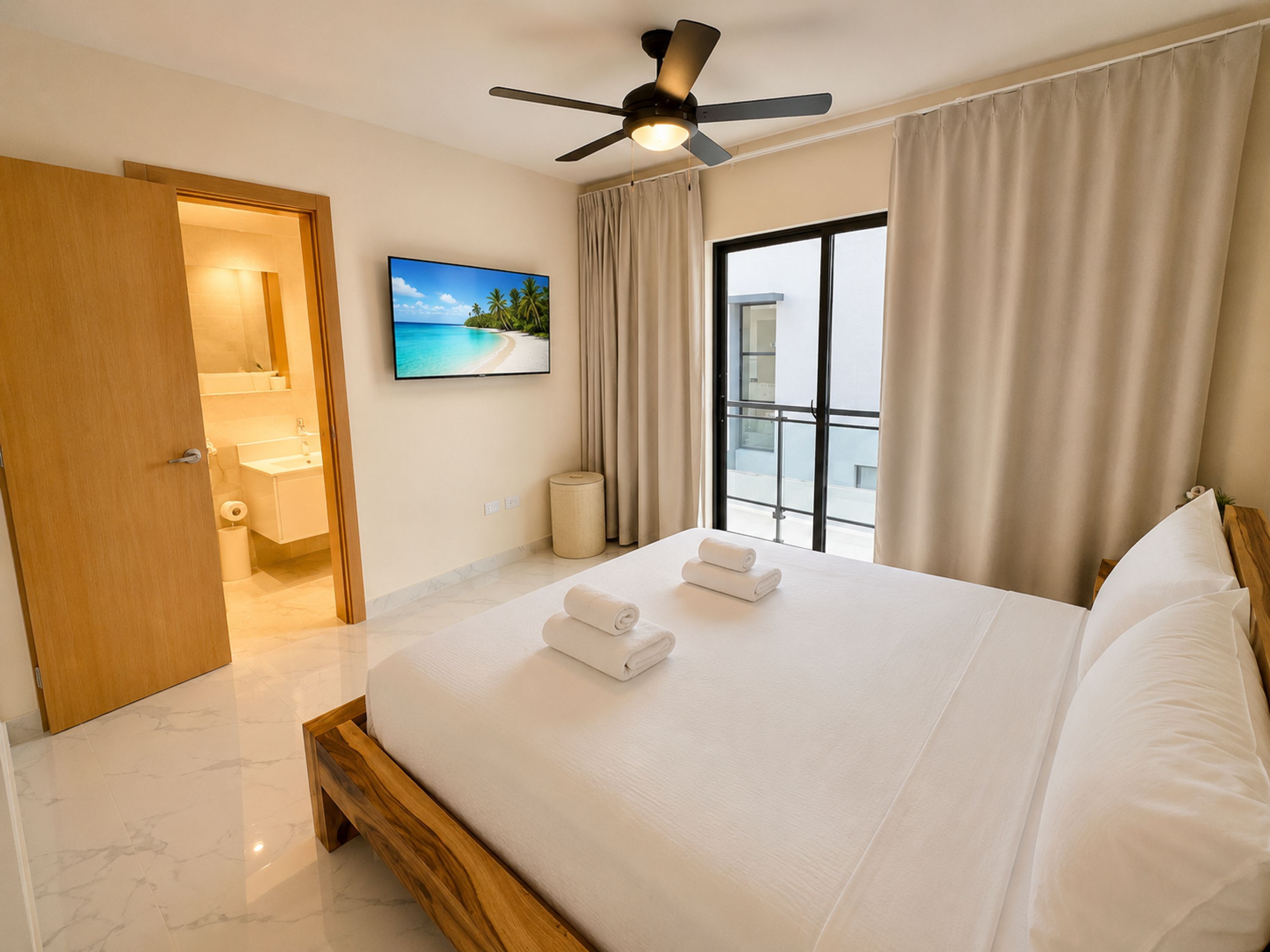 A hotel room with a bed, a ceiling fan, a TV, a bathroom with a sink and mirror, and a window with curtains.