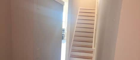 A narrow hallway with a dark wooden floor, white walls, and a staircase leading to an upper level.