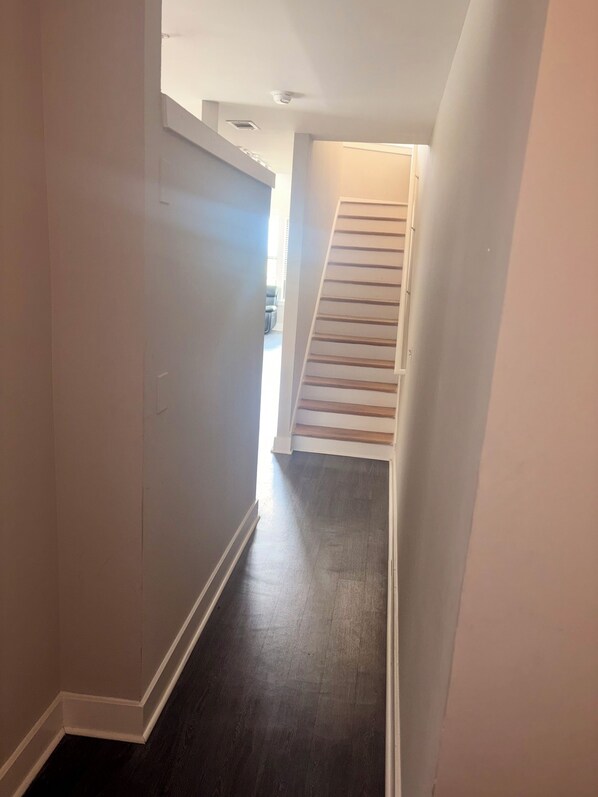 A narrow hallway with a dark wooden floor, white walls, and a staircase leading to an upper level.