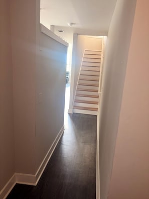 A narrow hallway with a dark wooden floor, white walls, and a staircase leading to an upper level.