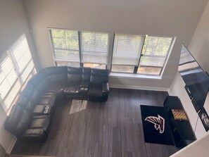 Una sala de estar moderna con un sofá modular, ventanas amplias con persianas y un logotipo de equipo deportivo en el suelo.