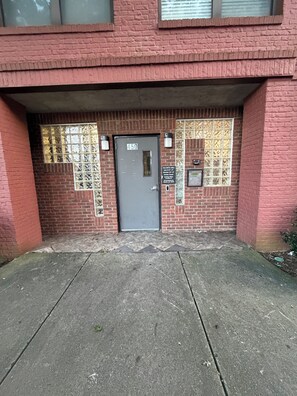 A building entrance with a numbered door, a security camera, and a sign with operating hours.