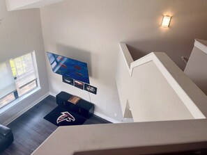 A modern living room with a flat-screen TV mounted on the wall, a black entertainment unit, and a wooden floor. - Game Day Get Away! Steps From Mercedes Benz stadium! (Atlanta)
