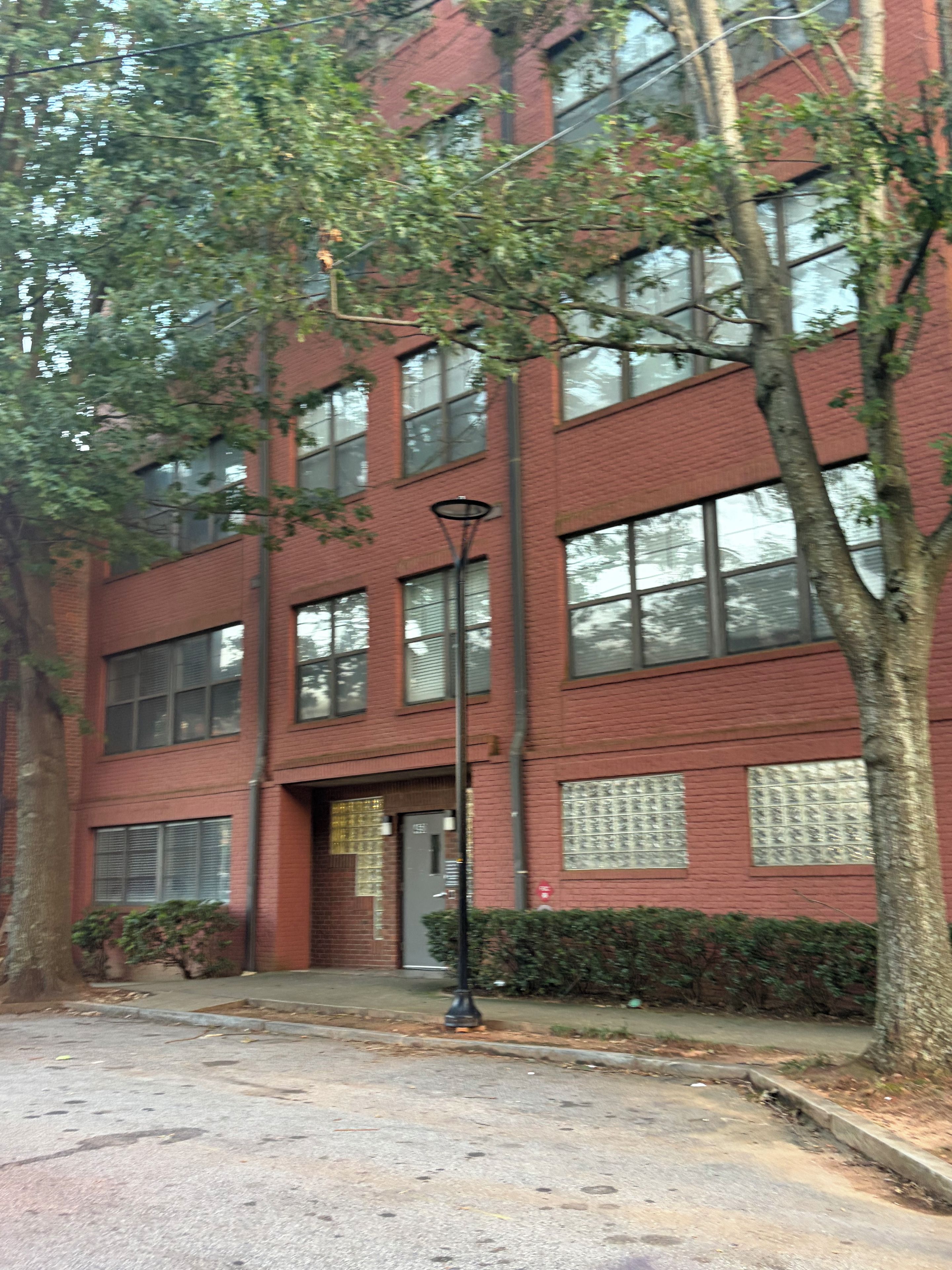 A red brick building with multiple windows, a black street lamp, and a tree in front.