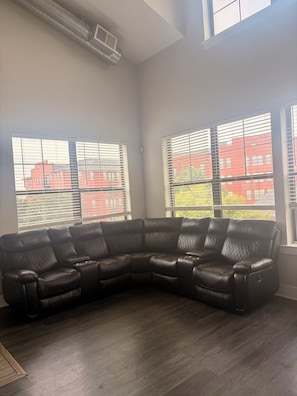 A corner living room with a sectional sofa, large windows with blinds, and a visible air conditioning vent. - Game Day Get Away! Steps From Mercedes Benz stadium! (Atlanta)