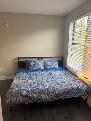 A bedroom with a bed, a window with blinds, and a wall socket.