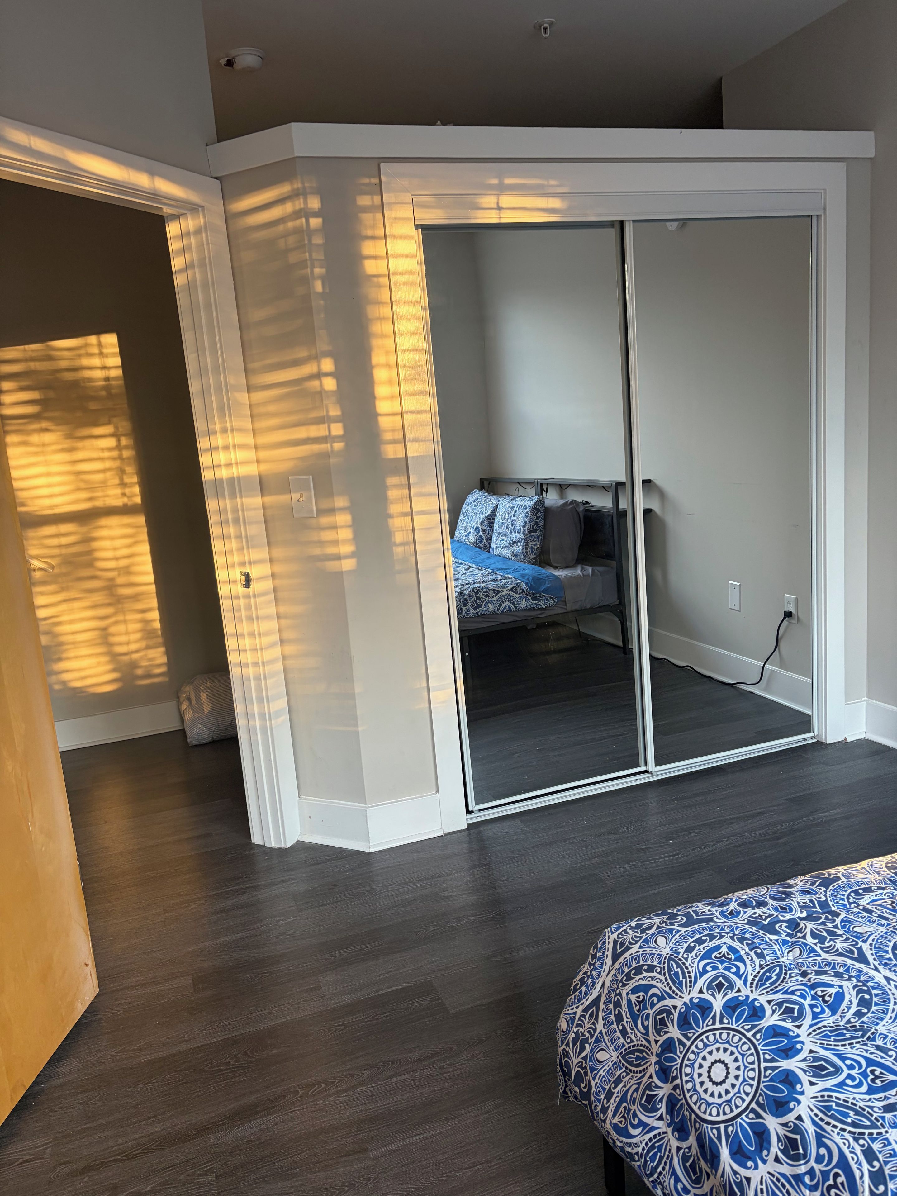 A bedroom with a sliding door closet, a bed with patterned bedding, and a dark wooden floor.