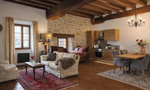 A cozy living room with a fireplace, a dining area with a wooden table, and a kitchen with stone walls.