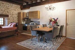 A cozy kitchen with wooden cabinets, a dining table with chairs, a chandelier, and a stone wall.