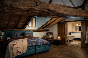 A bedroom with a sloped ceiling, a large bed, a chair, a nightstand, and a bathroom visible through an open door.