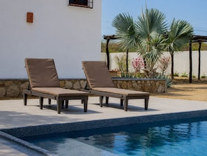 Un espace aménagé au bord de la piscine, avec deux chaises longues et un mur en pierre.