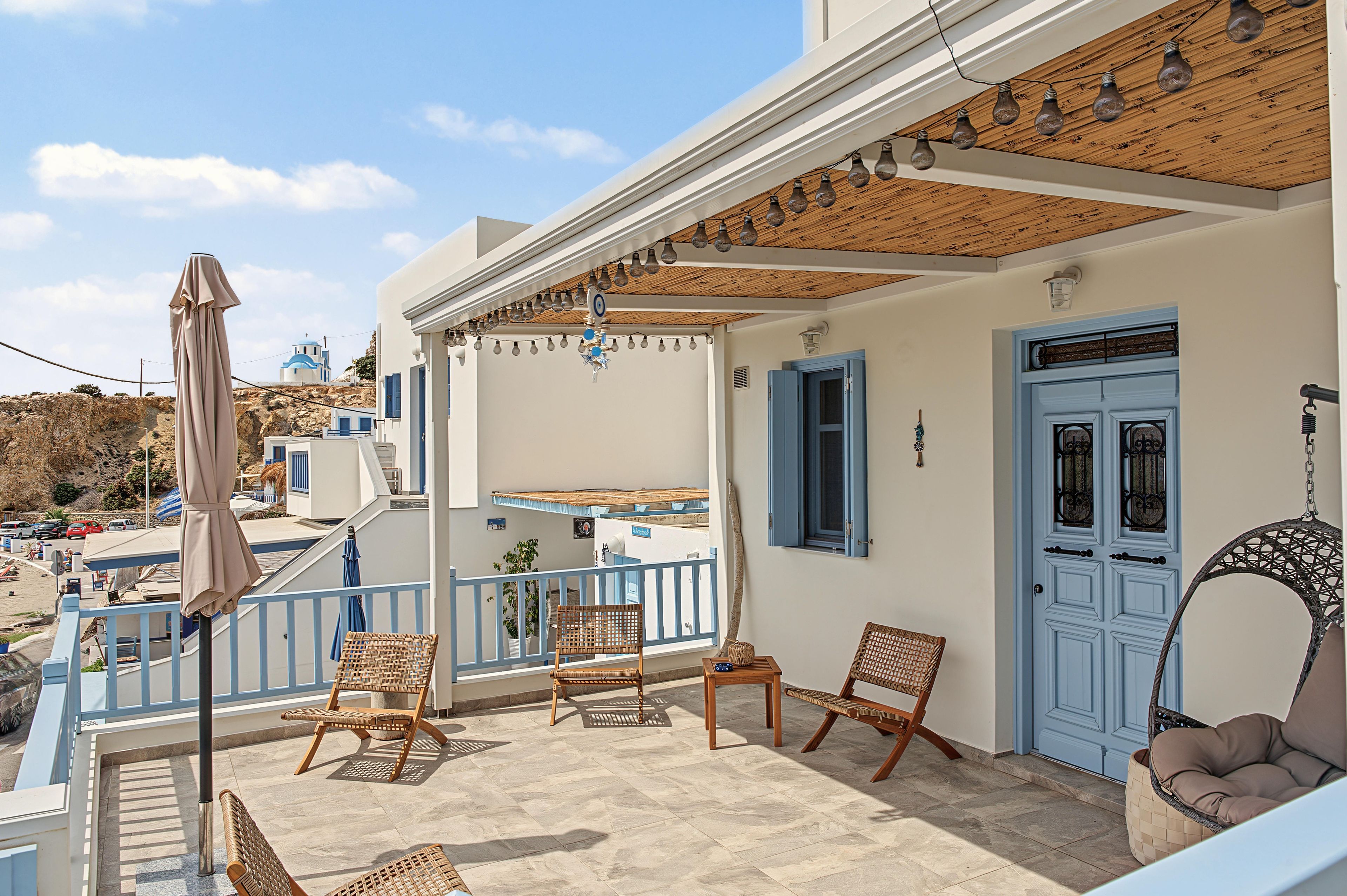 Un balcon agrémenté de meubles en osier, une porte bleue et une vue sur une colline.