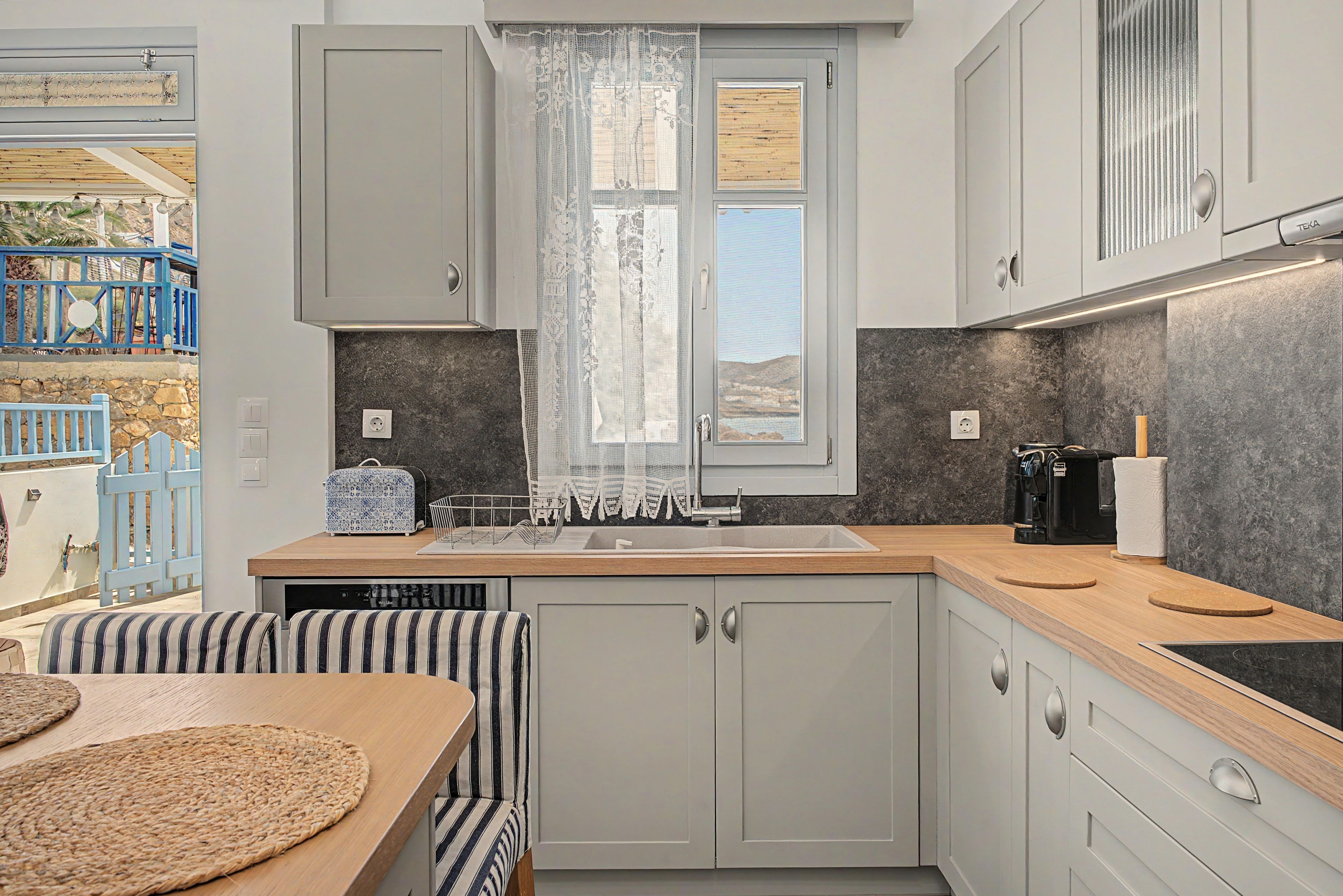 A modern kitchen with a built-in dishwasher, a coffee machine, and a view through a window with a lace curtain.