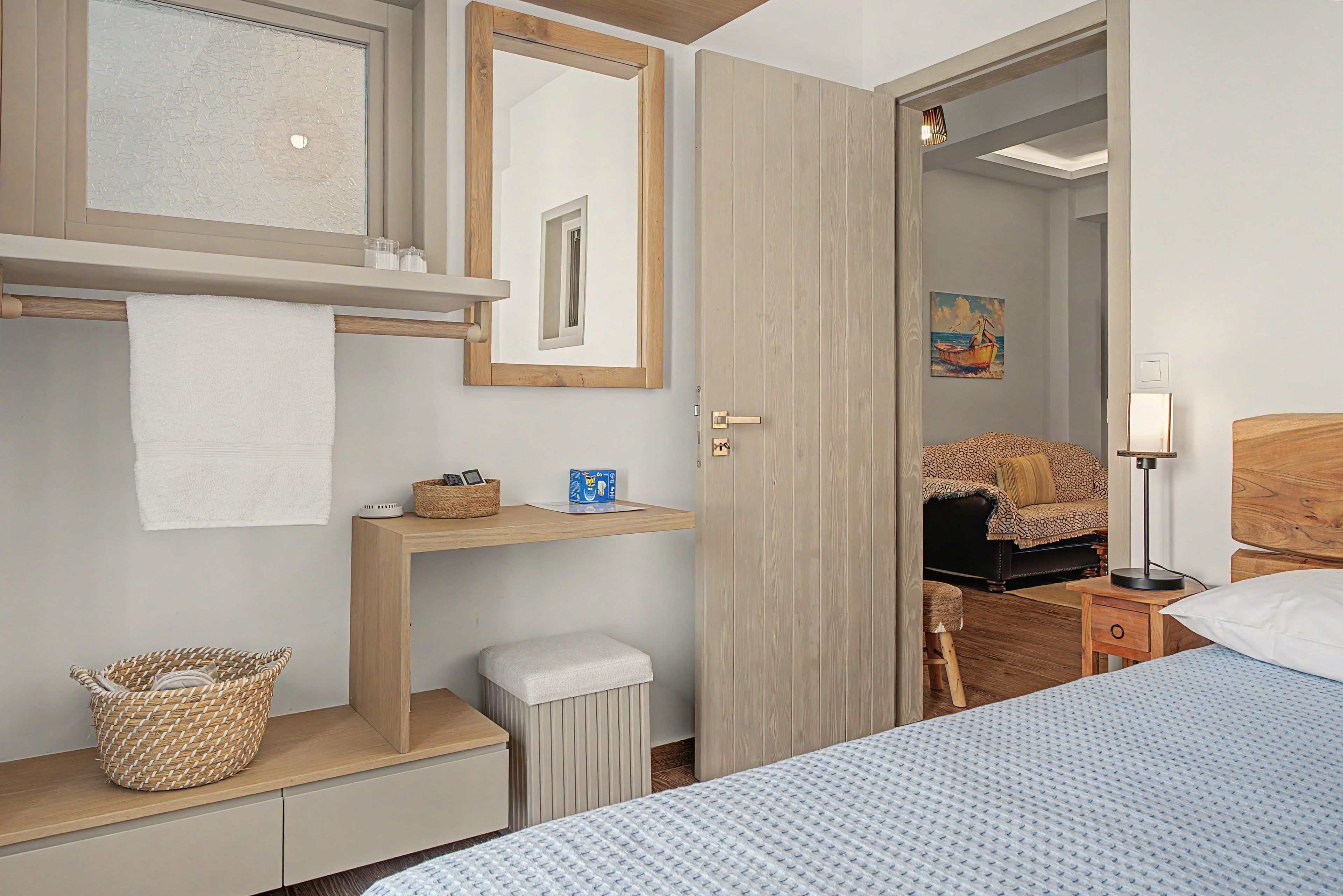 A bedroom with a bed, a bedside table, a nightstand, a mirror, a door, and a wall-mounted shelf.