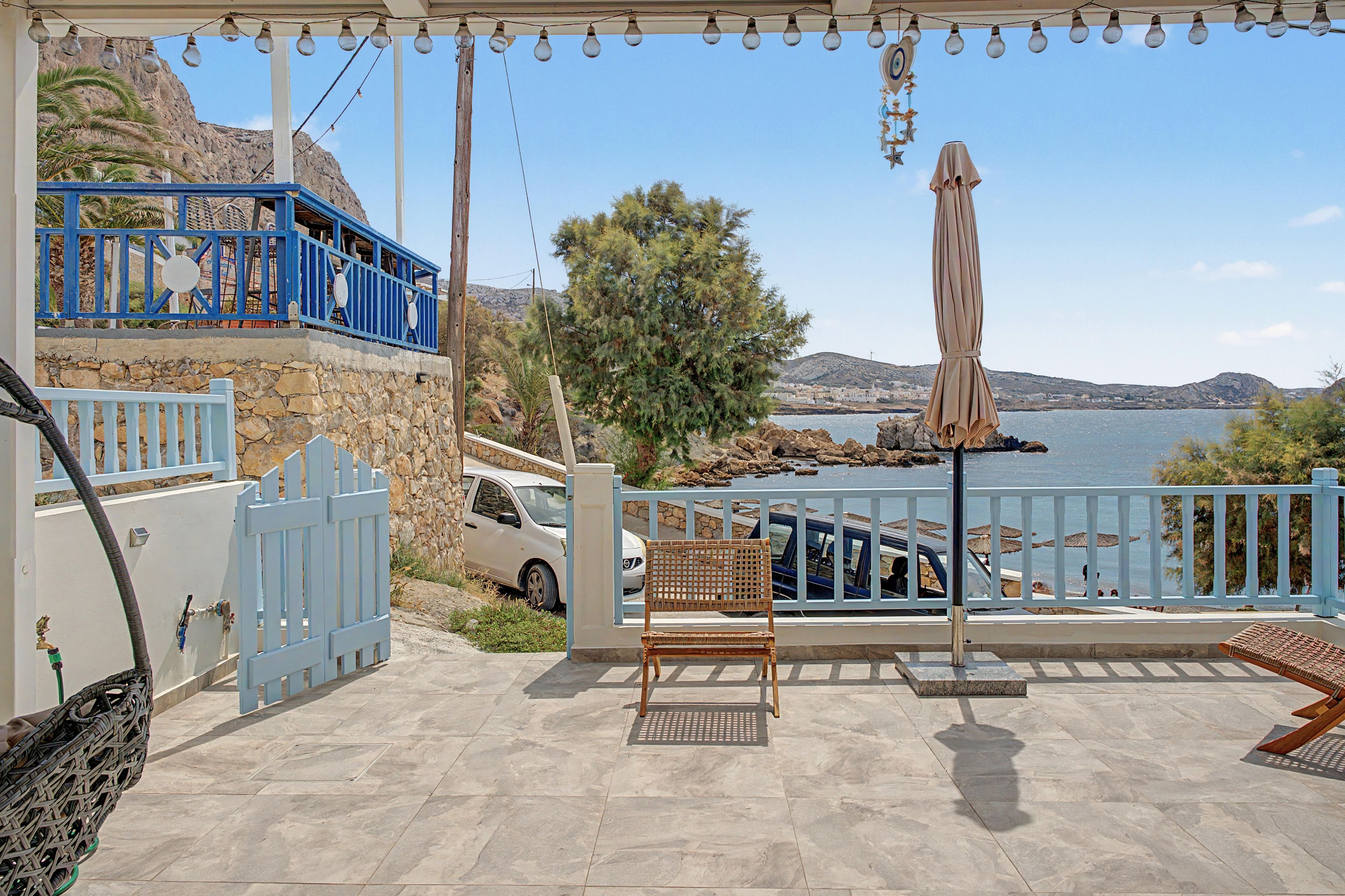 A covered outdoor seating area with a view of the sea, a stone wall, and a blue railing.