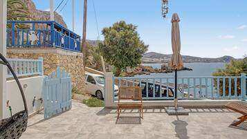 A covered outdoor seating area with a view of the sea, a stone wall, and a blue railing.