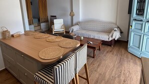Cozinha moderna com ilha de madeira, banquetas listradas e um sofá estampado numa sala de estar iluminada.