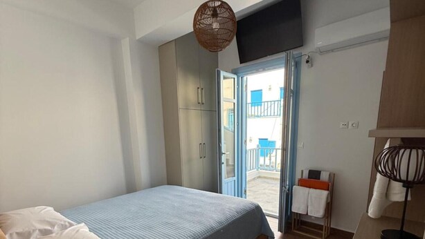 Quarto com cama, televisão, armário de madeira e vista para o exterior.