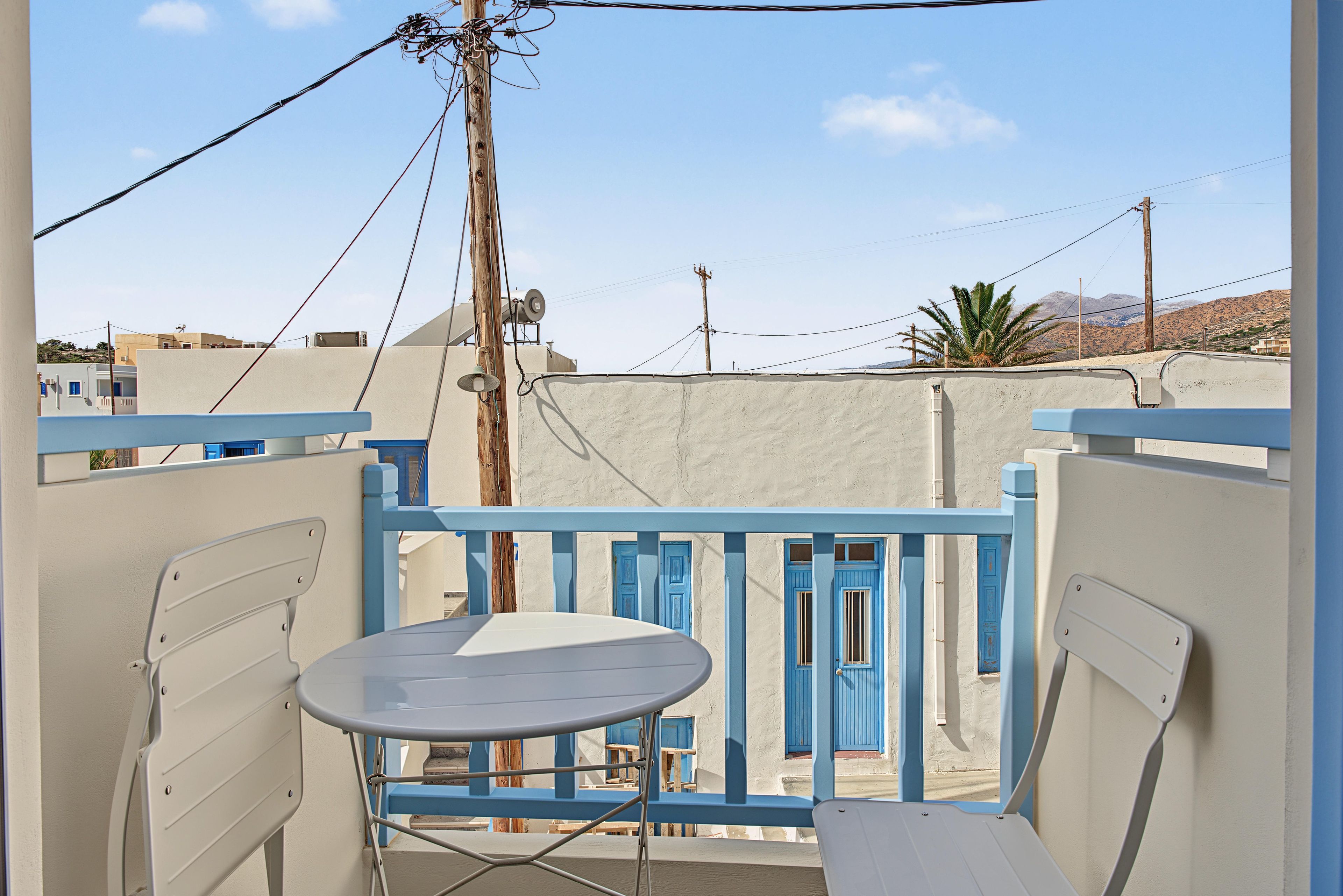 Een balkon met een tafel en stoelen, met uitzicht op een woongebied met gebouwen en een berg op de achtergrond.