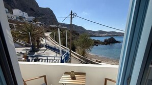 Un balcón con vista al mar, una mesa, dos sillas y una mesita con un florero.