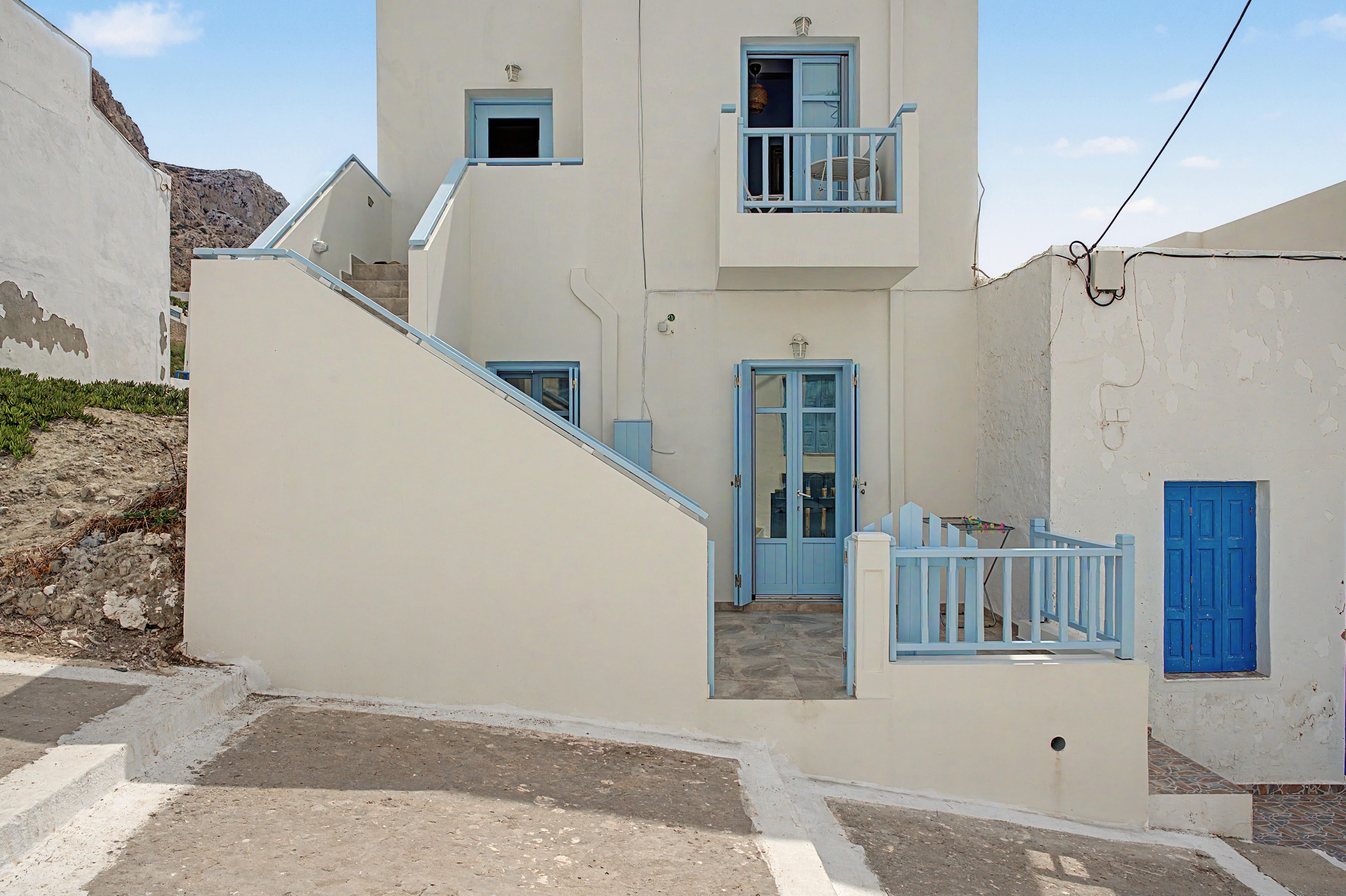 Ein zweistöckiges Gebäude mit einer Treppe zum Obergeschoss, einem Balkon mit blauer Brüstung und einer blauen Tür.